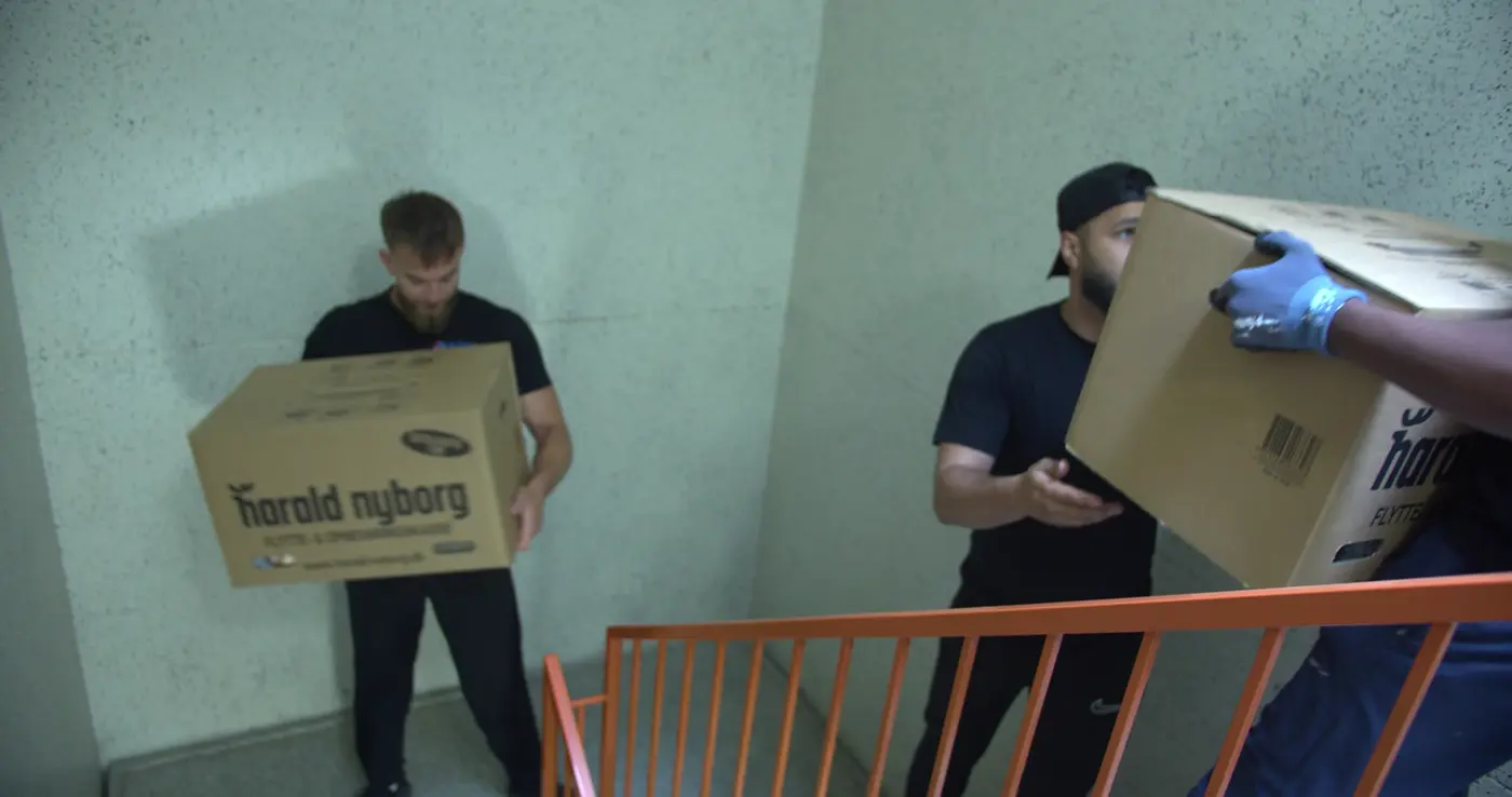 To flyttemænd bærer flyttekasser gennem en trappeopgang
