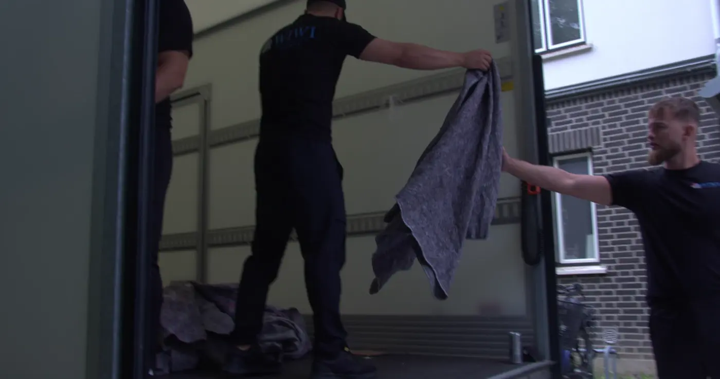 Flyttemænd rækker flyttetæpper til hinanden ved flyttebilen
